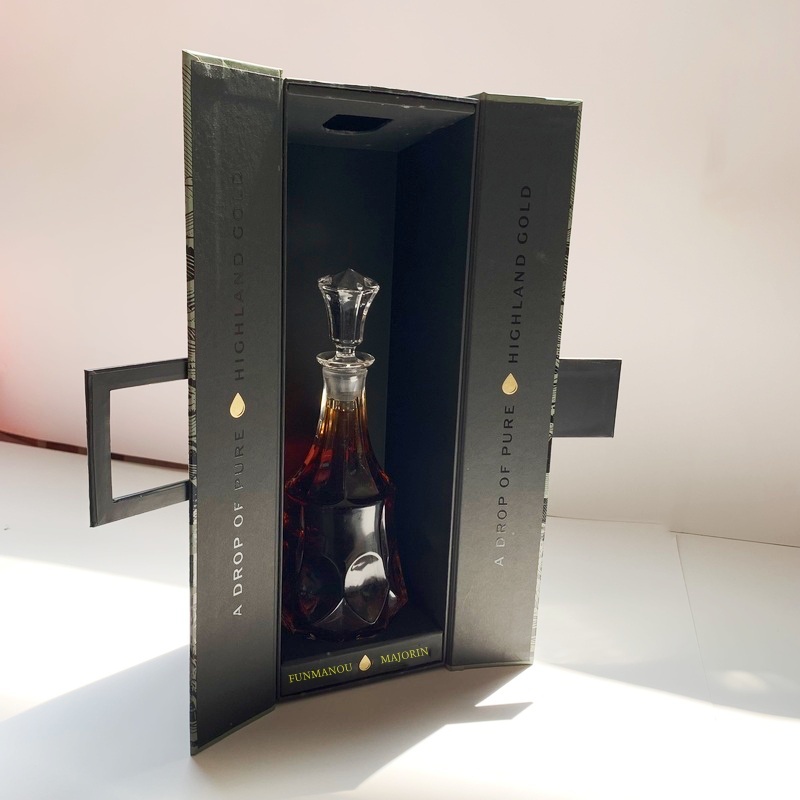 Black double-door rigid gift box with gold foil branding presenting a crystal bottle