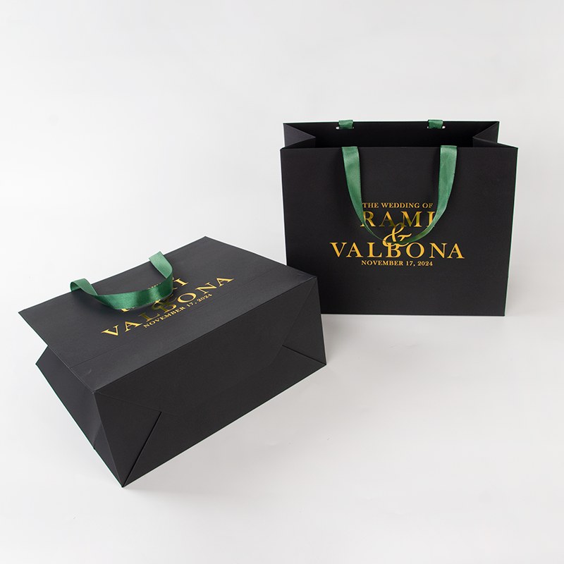Matte black luxury paper shopping bags with gold foil printing and green satin ribbon handles